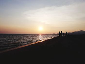 Silhouette people on beach against sky during sunset