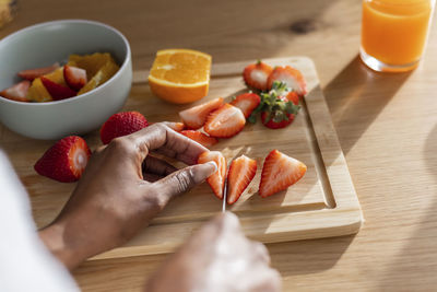 Hands of woman cutting fresh strawberries at table in kitchen