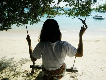 Rear view of woman on swing at beach