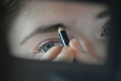 Cropped image of woman applying eyebrow pencil while reflecting on mirror