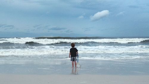 Rear view of boy standing with butterfly net on shore at beach