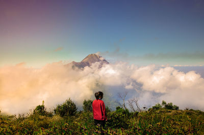 Rear view of woman standing on grassy field against mountain amidst clouds