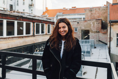 Portrait of smiling young woman standing against buildings