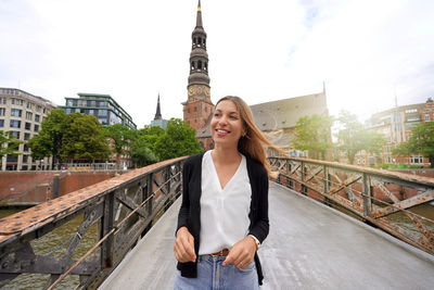 Portrait of smiling young woman walking on bridge in the city of hamburg, germany