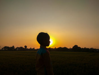 Boy standing on field against sky during sunset