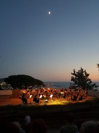 People by illuminated tree against clear sky at night