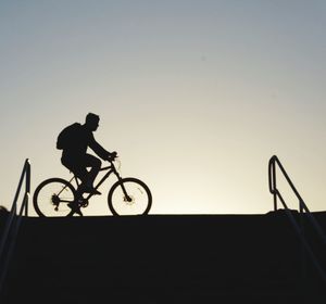 Silhouette man riding bicycle against clear sky