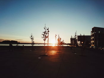 Silhouette city street against clear sky during sunset
