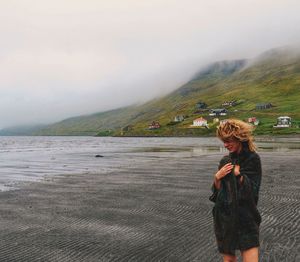 Woman standing on sand against sea during foggy weather