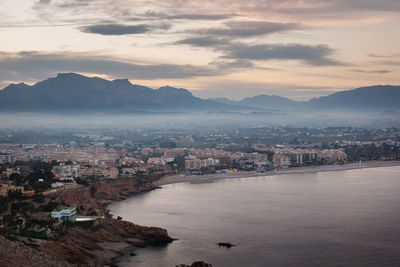 Aerial view of townscape by sea against sky