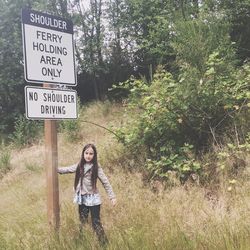 Portrait of girl standing by sign board with text on grassy field