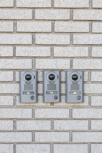 Three intercom on white textured brick wall, close up