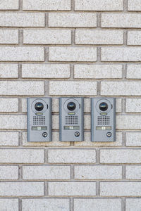 Three intercom on white textured brick wall, close up