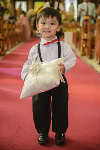 Cute boy holding gift while standing on red carpet