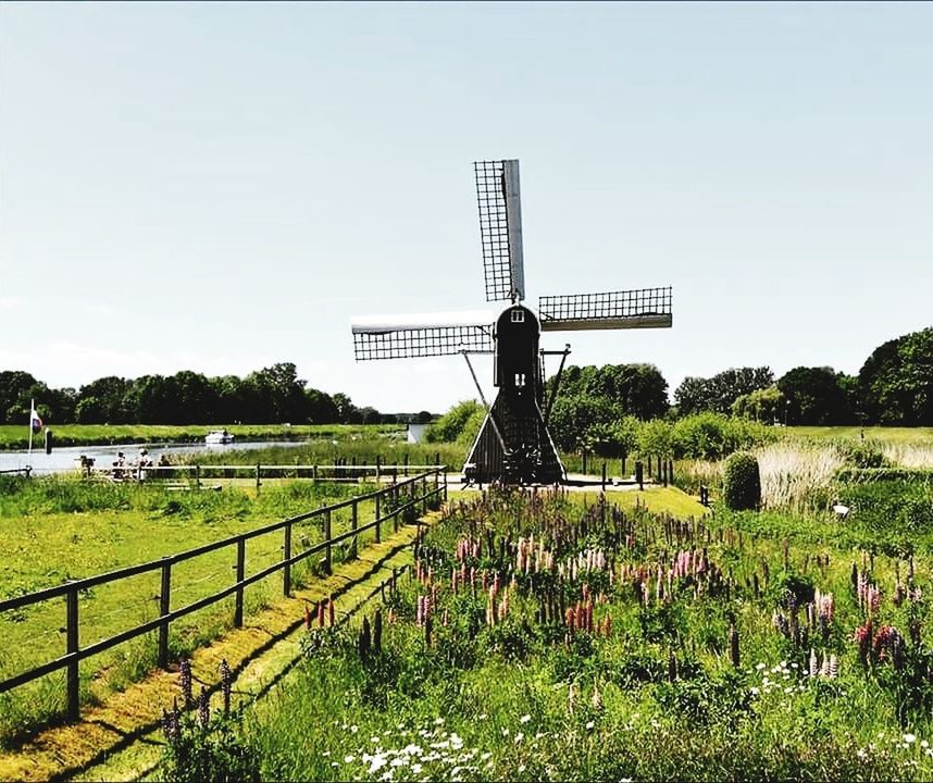 TRADITIONAL WINDMILL ON FIELD BY BUILT STRUCTURE AGAINST SKY