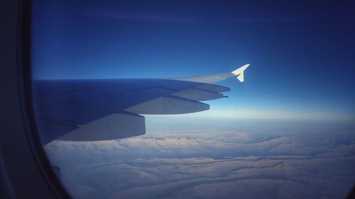 Cropped image of airplane flying over sea against blue sky