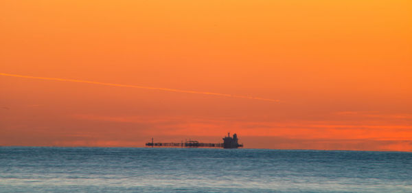 Silhouette boat in sea against orange sky