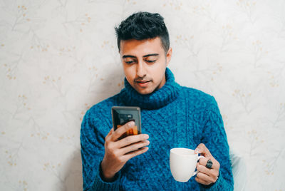 Young man using mobile phone against wall