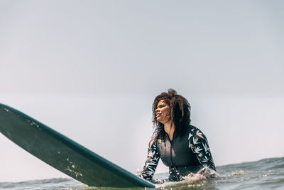 Black woman sitting on her surfboard in the water