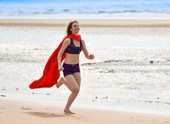 Full length of young woman wearing cape while running at beach