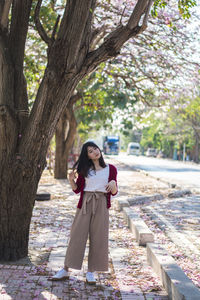 Full length of young woman with head cocked standing by tree