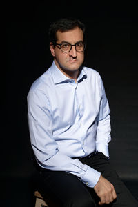 Portrait of young man sitting against black background