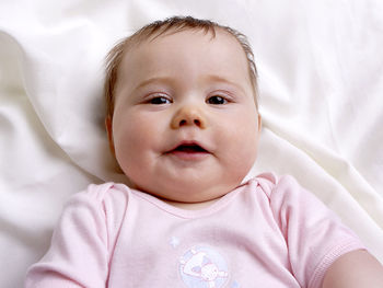 Baby girl lying on a white blanket looking into the camera