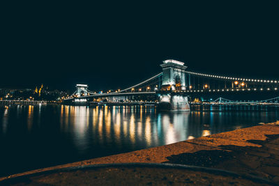 Illuminated golden gate bridge over river against sky at night