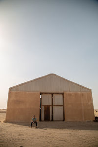 Rear view of man standing by building against clear sky