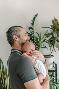 Dad holding his new born baby son in room with green plants
