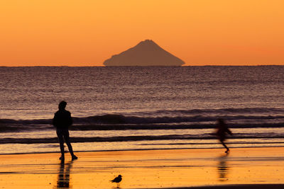 Silhouette people standing on beach against orange sky