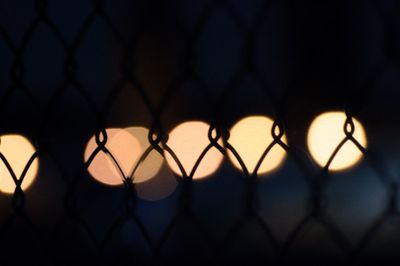 Close-up of silhouette chainlink fence against lens flare