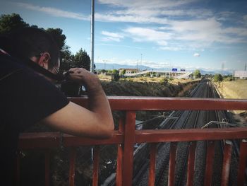Man photographing railroad tracks from bridge