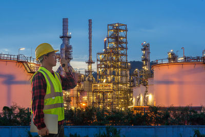 People standing at illuminated factory against sky at night