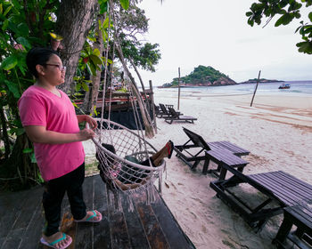 Young girl standing near the beach swing or hammock and white sand and calm sea.