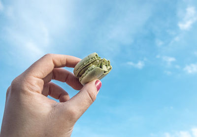 Close-up of hand holding macaroon against blue sky