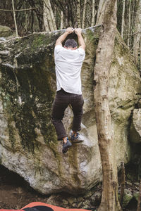 Full body of a male rock climber climbing a rock in a forest