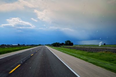 Empty road amidst field against cloudy sky during sunset