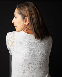 Young woman looking away while standing against black background