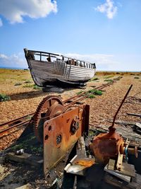 Old rusty machinery and fishing boat on shingle beach against sky