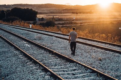 Rear view of mid adult man walking on railroad track against sky