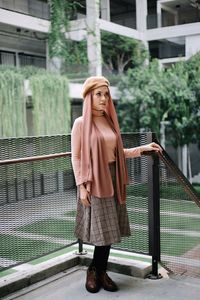 Full length portrait of young woman standing against railing