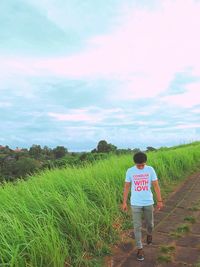 Rear view of man standing on grass against sky