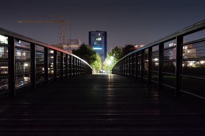 Illuminated footbridge amidst buildings in city at night