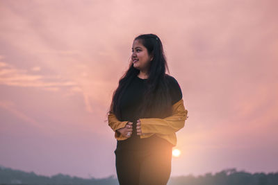 Young woman standing against orange sky