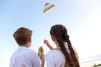 A girl and a boy launch a bright kite into the sky, a view from the back.