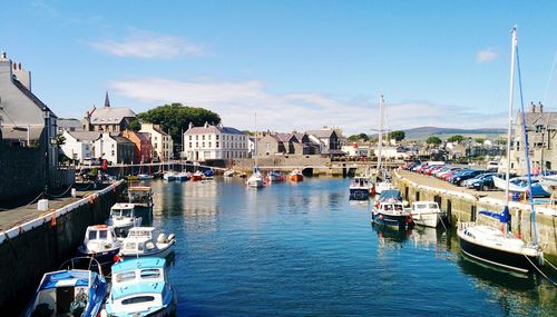 Boats moored at harbor against blue sky in city