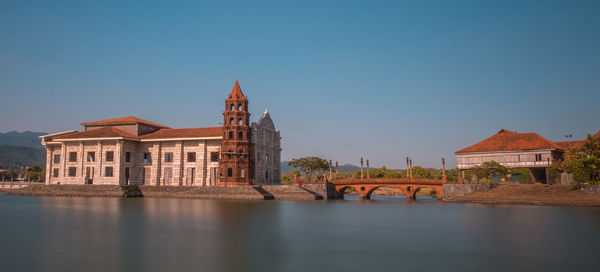 View of buildings by river against clear blue sky