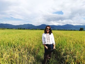 Portrait of smiling young woman standing on field against sky