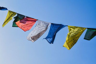 Low angle view of flags against clear blue sky